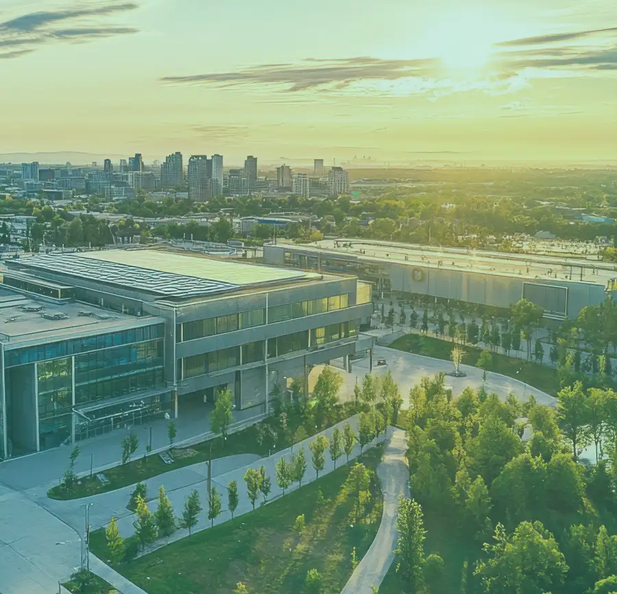 Large building structure with green trees and pathways with the skyscrapers in the distance